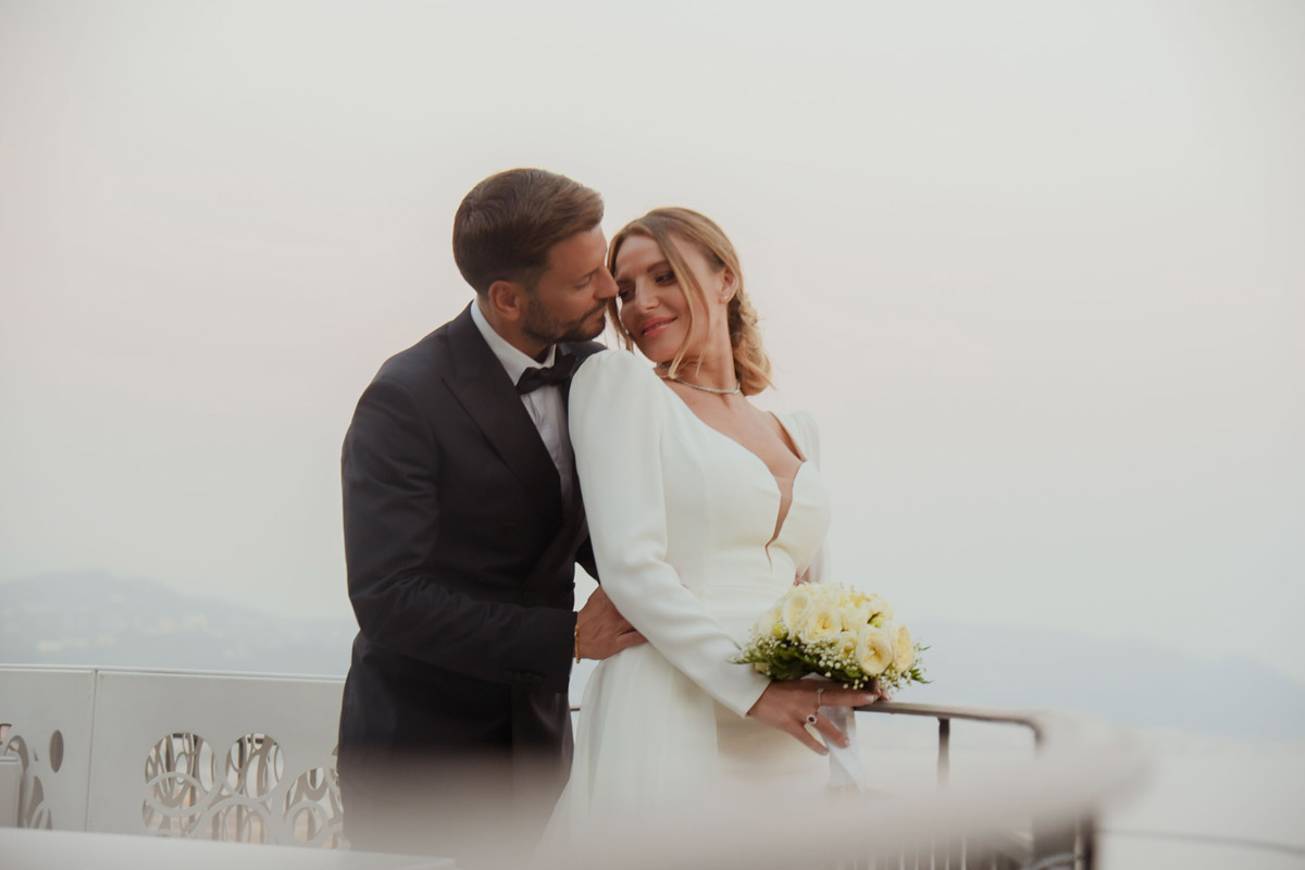 Sposi abbracciati sulla terrazza al tramonto con bouquet, matrimonio vista mare Costiera Amalfitana